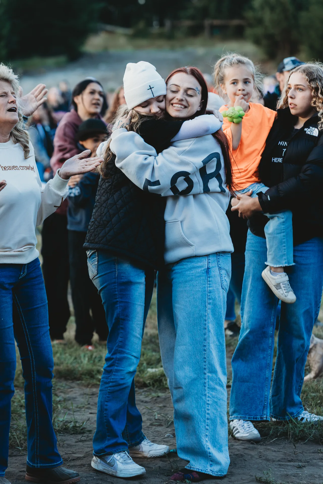Two women embracing in worship as the crowd gathers around